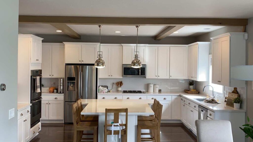 A modern kitchen with white cabinets, stainless steel appliances, a central island with wooden chairs, and pendant lighting.
