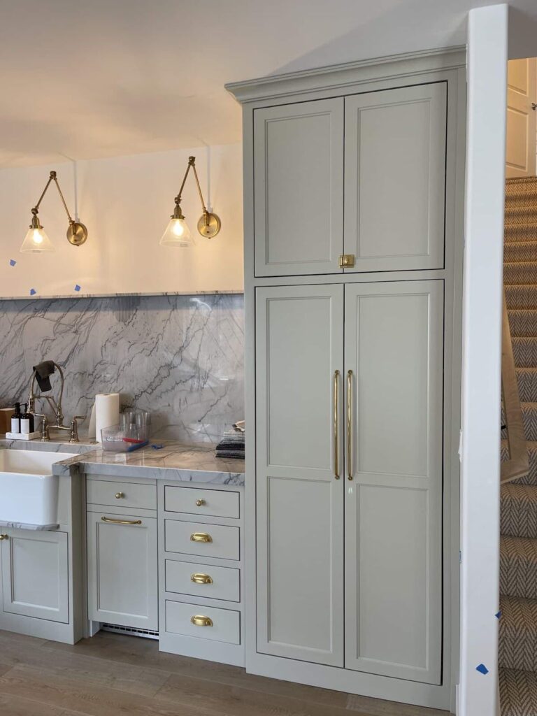 Modern kitchen with marble backsplash, brass hardware, and tall pantry cabinets.